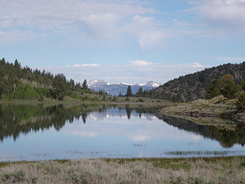view of small lake with hills along side and mountains in the distance
