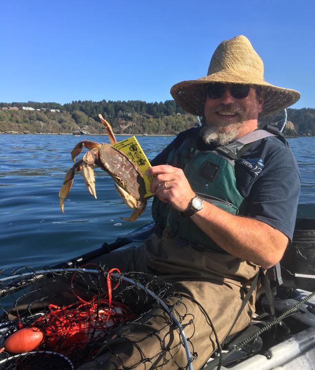 scientist on a boat in water with Dungeness crab and tool