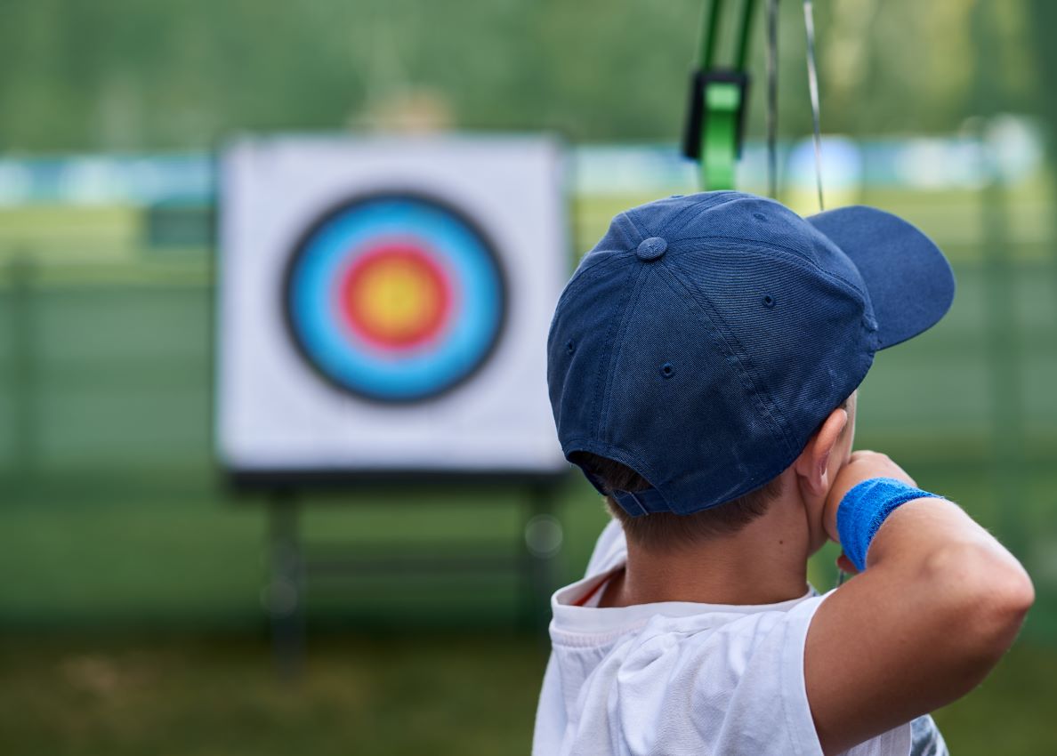young person drawing back an archery bow with target in background