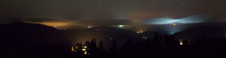distant hills at night, with light coming from a far away city shining through the nighttime clouds