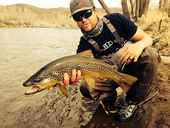 man holding large spotted fish on river bank