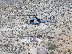 Helicopter in air delivering water which is surrounded by mountain