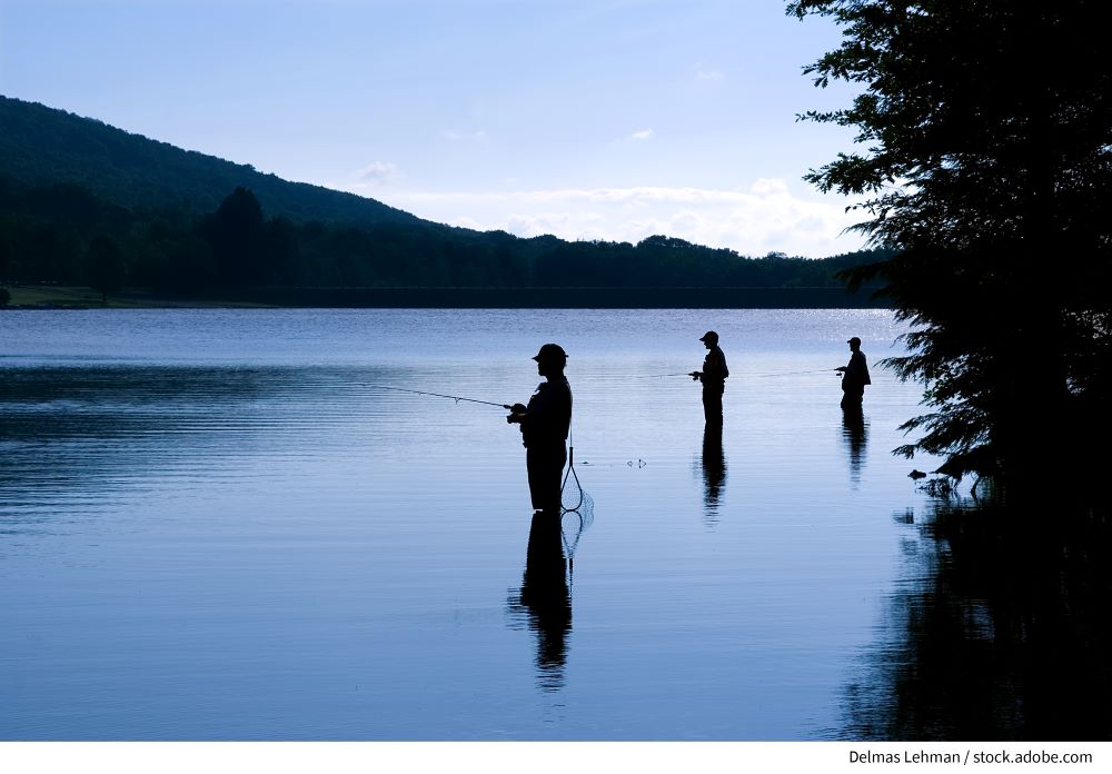 Two people in silhouette fishing in a river at day break with mountains in the background