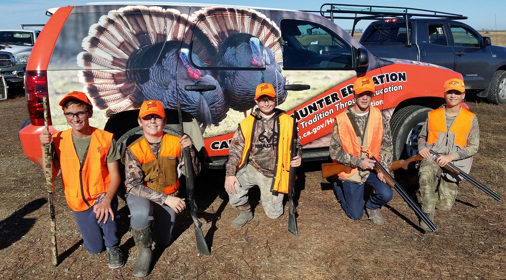 Five youth hunters kneeling in front of a CDFW Hunter Education van