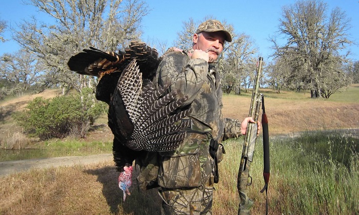 Lake County Chief Deputy District Attorney Richard Hinchcliff, avid turkey hunter, afield dressed in camo holding a shotgun with a dead turkey slung over his shoulder