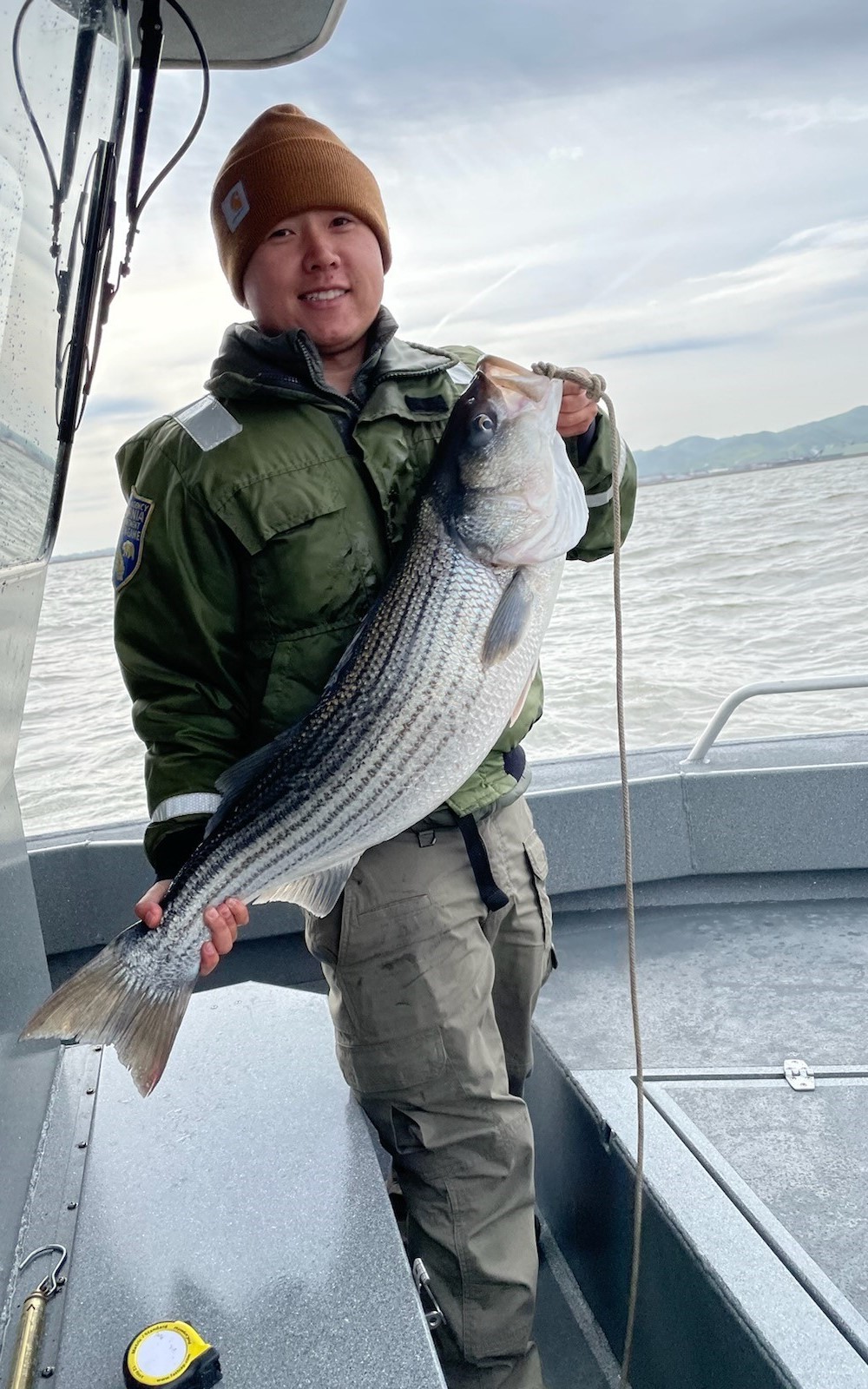 Smiling man on a boat holding up a large striped bass