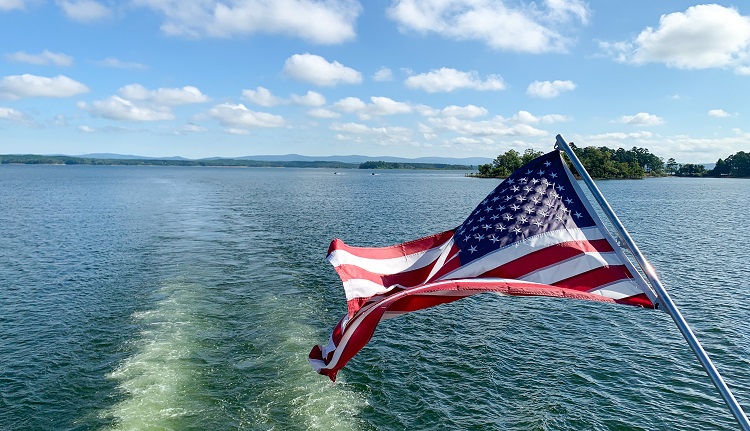 An American flag flaps off the stern of a boat on a lake.