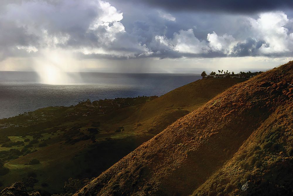 Hills with ocean and sun shining through clouds