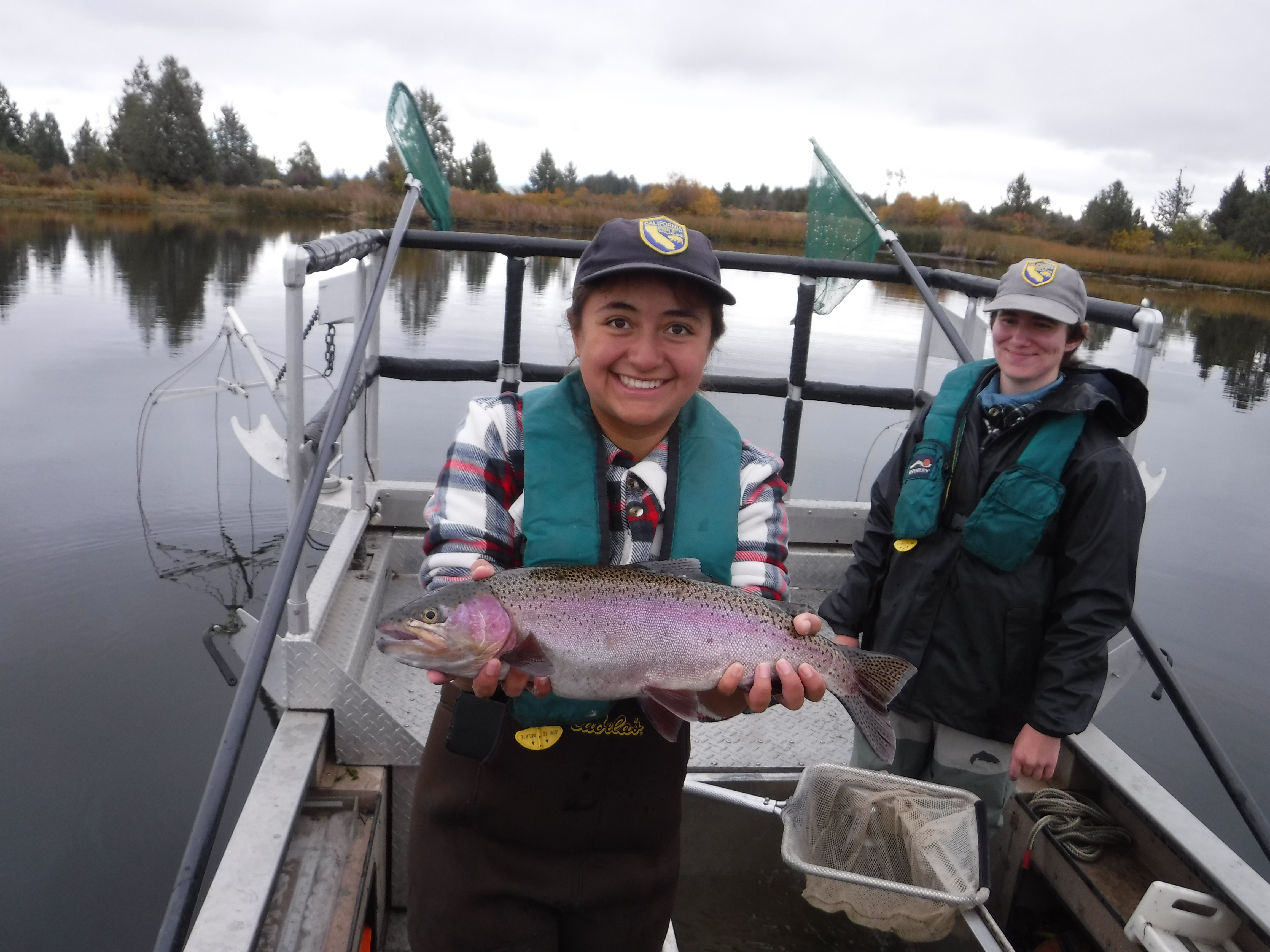 Monica standing on an electrofishing boat smiling and holding a large trout