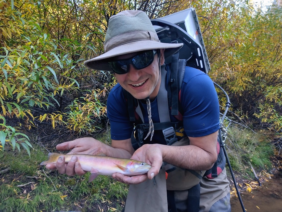 Sebastian Ayala crouching down holding a trout