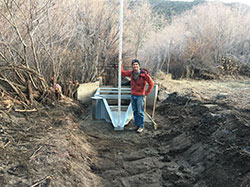 Scientist, Aaron Johnson, standing in a trench in dirt with tall dry trees in background