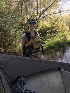 Scientist, Whitney Albright standing on the river bank next to a boat with a life jacket