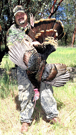 male hunter in camouflage, holding large, dead, wild turkey