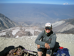a female backpacker wearing a baseball cap sits on a barren slope of Mt. St. Helens