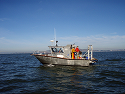 small aluminum research vessel on calm bay water, with two men wearing orange dry suits