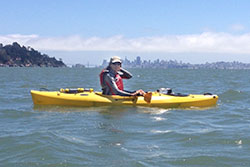 scientist on kayak in the ocean with trees and blue sky in the background