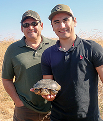 Two men in a marsh, one holds a turtle