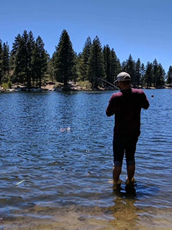 Scientist, Roy Kim, fishing in a lake with tall trees and blue sky in background