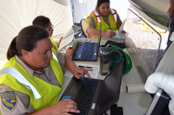 three women type on laptop computers in a tent