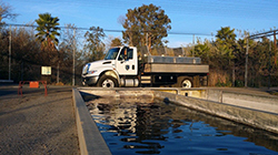 a tank truck parked next to a concrete fish hatchery raceway with palm trees in background