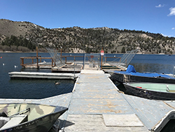 Dock on lake with small fishing boats. Mountainside with trees in background.