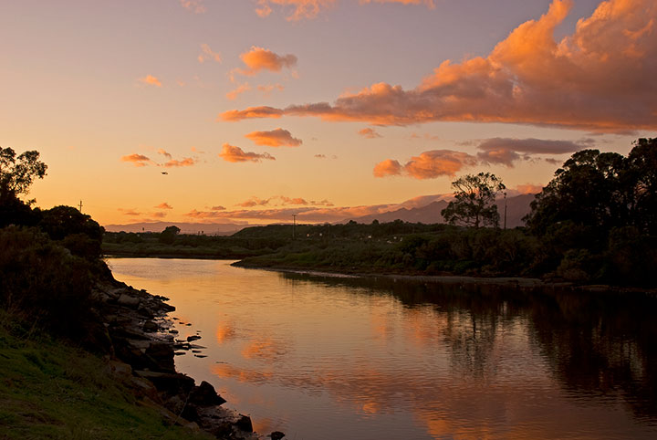 calm water along steep shoreline reflects clouds during a vibrant sunset