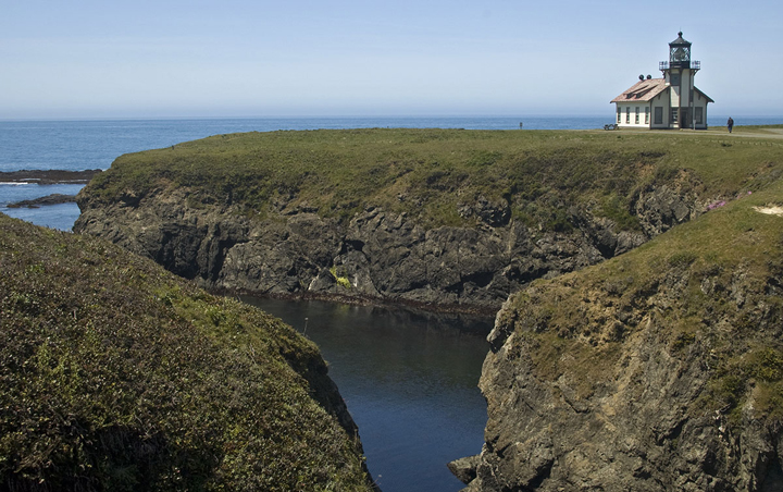 small light house sits on a bluff overlooking ocean