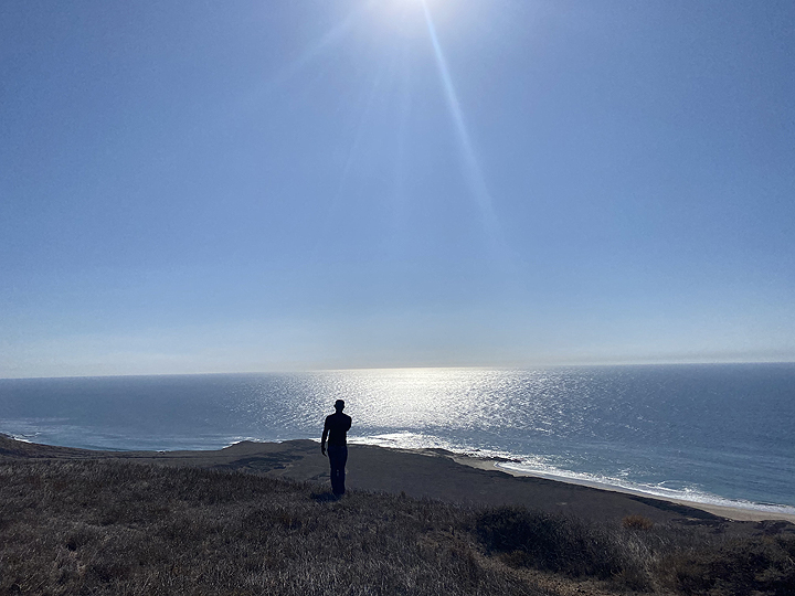 lone human figure silhouetted against the sun and sea