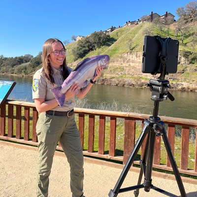 Image of female educator holding stuffed animal salmon to teach next to a river