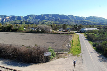road leading past farm field to hatchery buildings, with mountains in background