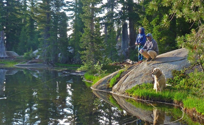 people on a rock, fishing in lake, with dog