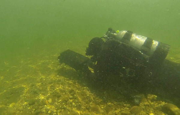 SCUBA diver near river bottom holding black device