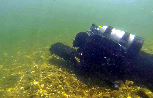 SCUBA diver near river bottom holding black device