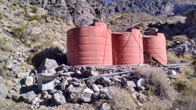 Three large plastic tanks hold water in the desert, and are connected to a metal drink box where the sheep drink from.