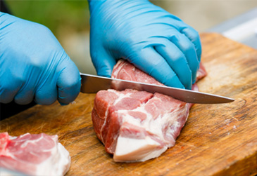 person's blue-gloved hands cutting meat on wood